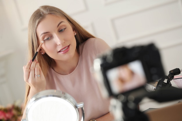 Foto gratuita vlogger de belleza. mujer joven grabando un tutorial de maquillaje