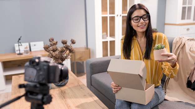 Vlogger femenina en casa con planta de unboxing de cámara