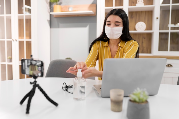 Vlogger femenina en casa con portátil y desinfectante de manos