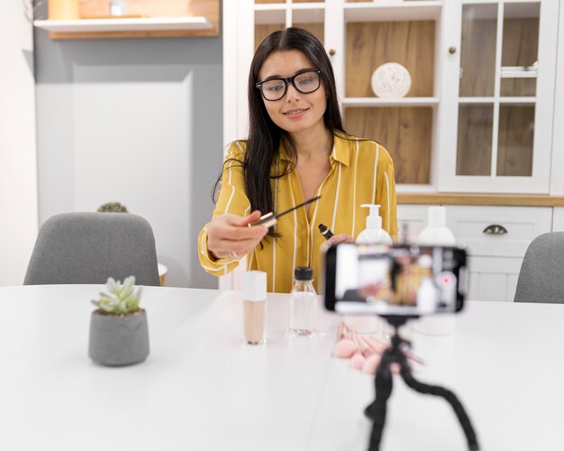 Vlogger femenina en casa con smartphone y productos respaldados