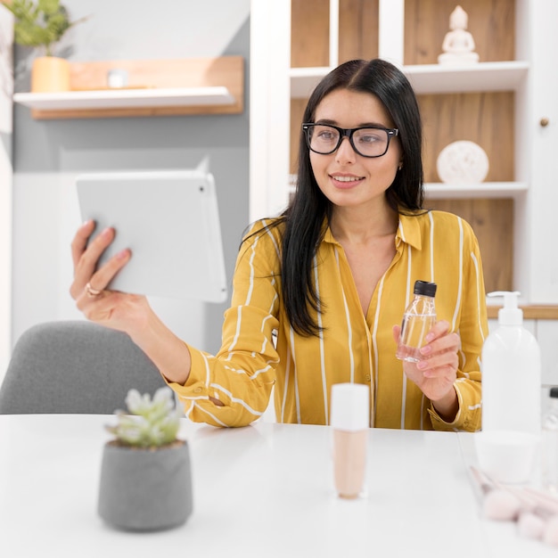 Vlogger femenina en casa con tableta y productos respaldados