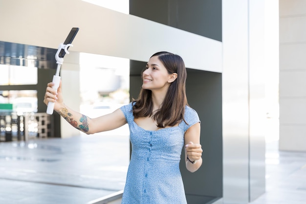 Vlogger sonriente grabando video en un teléfono inteligente mientras está de pie en un centro comercial