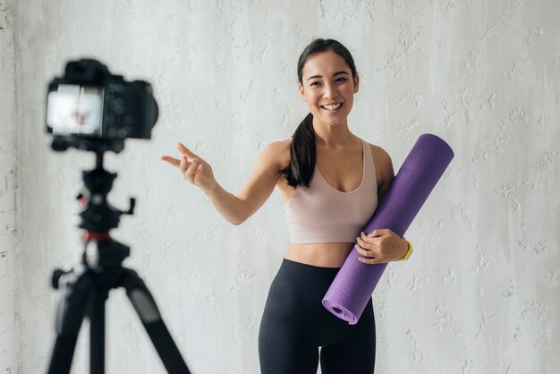 Foto gratuita vlogger sonriente sosteniendo una colchoneta de fitness