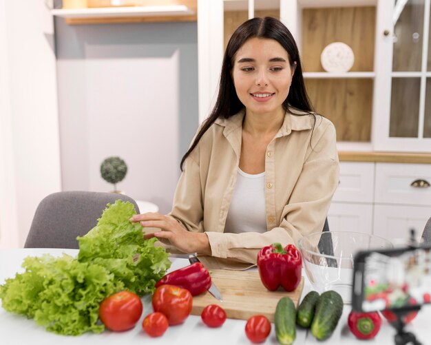 Vlogging femenino en casa con verduras y smartphone