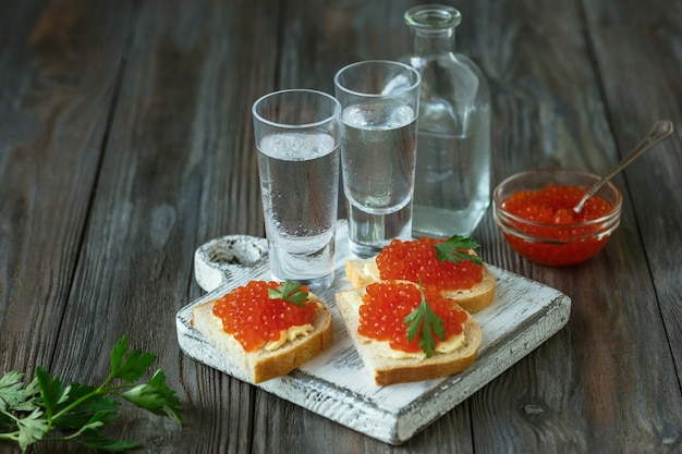 Vodka con caviar de salmón y tostadas de pan sobre mesa de madera