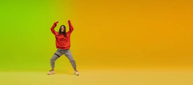 Volantes. Chica deportiva con estilo bailando hip-hop con ropa elegante en colores en el salón de baile con luz de neón.