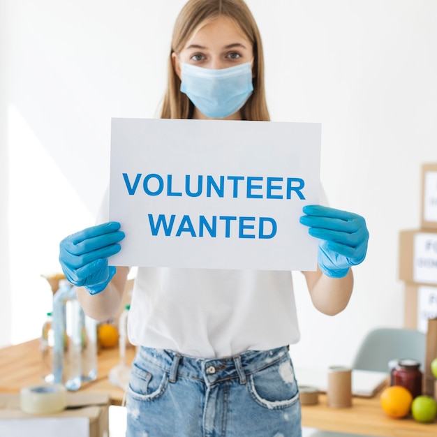 Foto gratuita voluntaria femenina con máscara médica y guantes sosteniendo papel con información