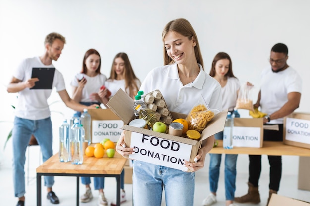 Voluntaria sonriente sosteniendo donaciones de alimentos en caja