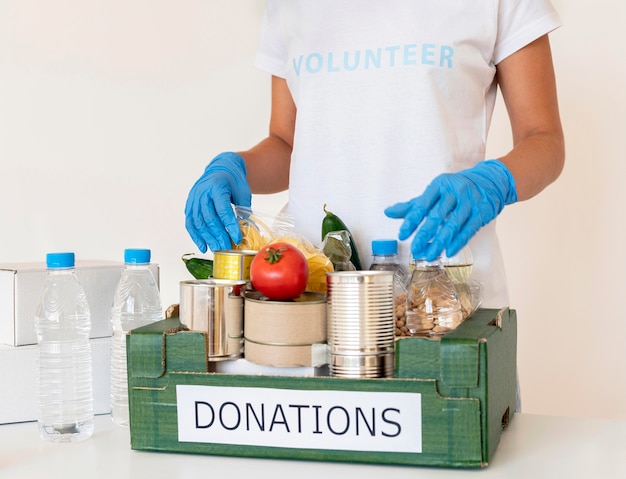 Voluntariado con guantes manejando caja de donaciones de alimentos