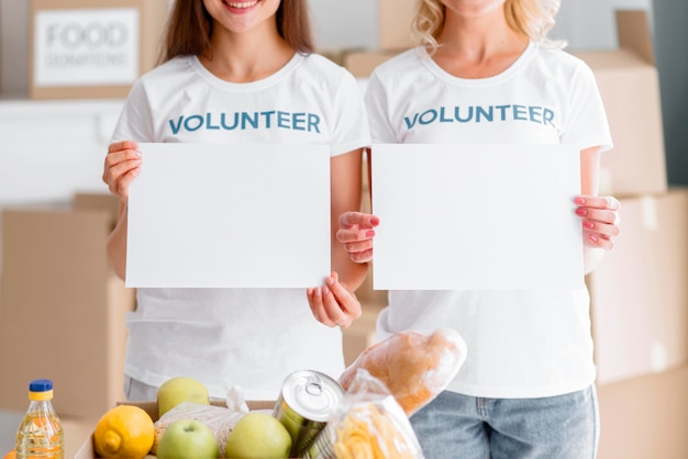 Foto gratuita voluntarias sonrientes posando con pancartas en blanco y donaciones de alimentos