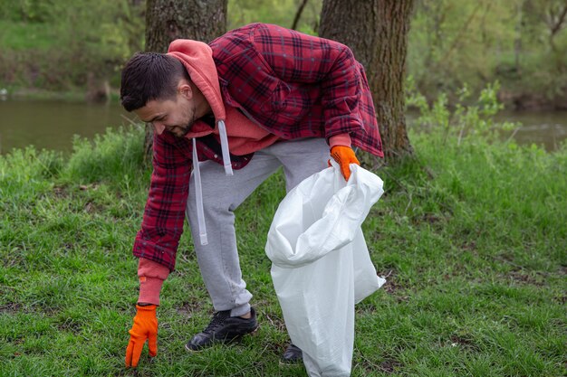 Un voluntario masculino con una bolsa de basura limpia el medio ambiente en el bosque.