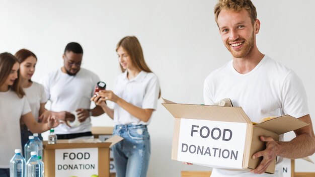Voluntario masculino sonriente con caja de donaciones de alimentos