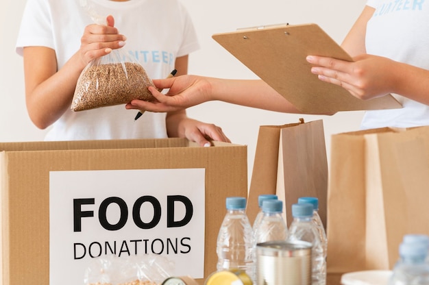 Foto gratuita voluntarios revisando alimentos para donaciones con bloc de notas