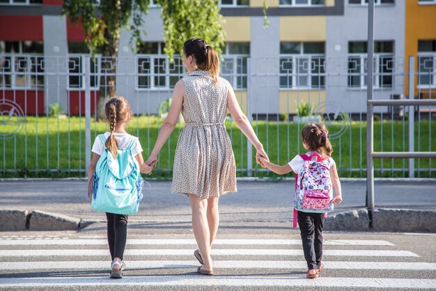 Volver al concepto de educación escolar con niñas, estudiantes de primaria, llevando mochilas para ir a clase tomados de la mano juntos caminando