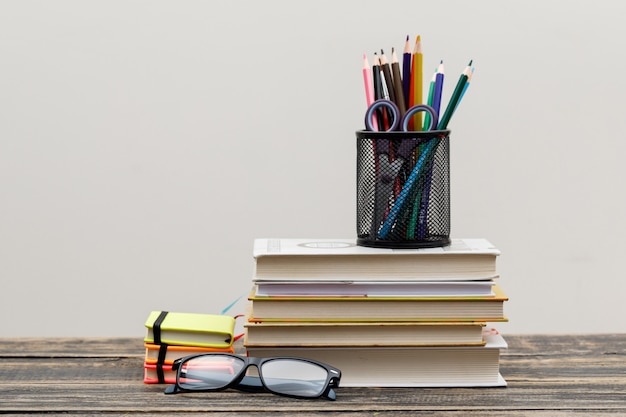 Volver al concepto de escuela con gafas, artículos escolares en vista lateral de pared de madera y blanco.