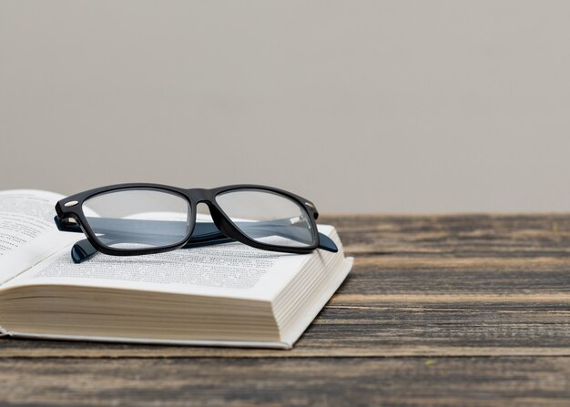 Volver al concepto de escuela con gafas en libro en vista lateral de pared de madera y blanco.