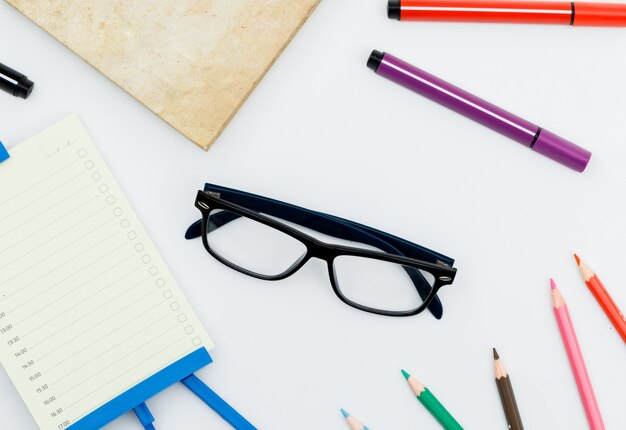 Volver al concepto de escuela con gafas, útiles escolares, planificador diario en mesa blanca plana.