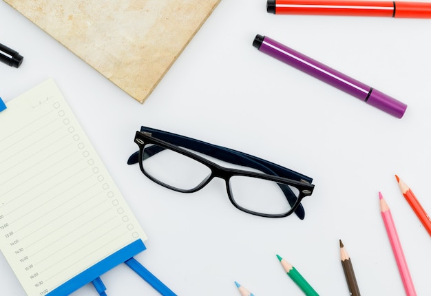 Volver al concepto de escuela con gafas, útiles escolares, planificador diario en mesa blanca plana.