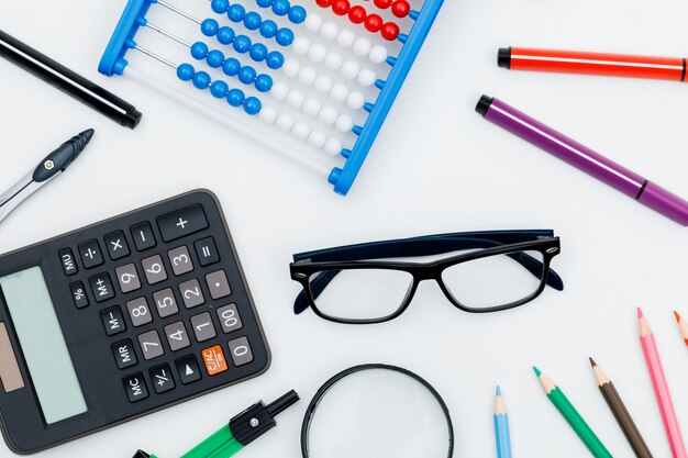 Volver al concepto de escuela con lupa, gafas, útiles escolares, calculadora en la pared blanca plana.