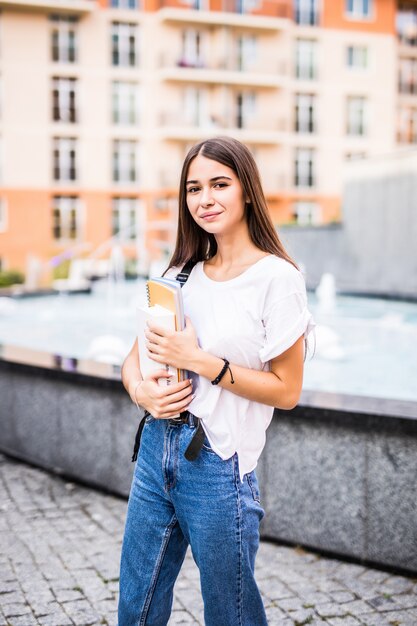 Volver a la escuela estudiante adolescente chica sosteniendo libros y cuadernos con mochila. Retrato al aire libre de la joven muchacha morena adolescente con el pelo largo. niña en la ciudad