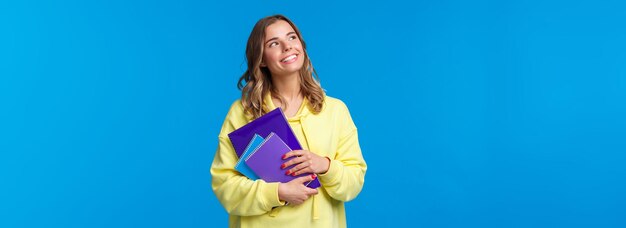 Volver a la escuela linda rubia sonriente estudiante europea llevar cuadernos y mirar material de aprendizaje