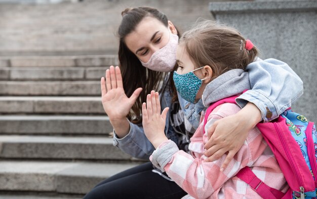 De vuelta a la escuela. Los niños de la pandemia de coronavirus van a la escuela con máscaras. Relaciones amistosas con la madre. Educación Infantil.