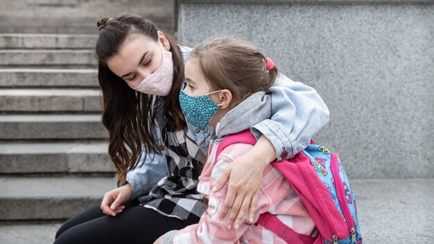 De vuelta a la escuela. Los niños de la pandemia de coronavirus van a la escuela con máscaras. Relaciones amistosas con la madre. Educación Infantil.