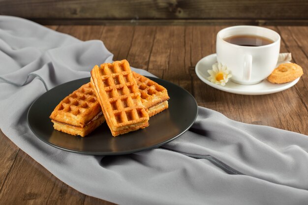 Waffles belgas en bandeja negra y una taza de té