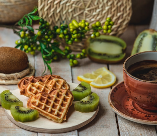 Waffles belgas en forma de corazón con rodajas de kiwi y una taza de café
