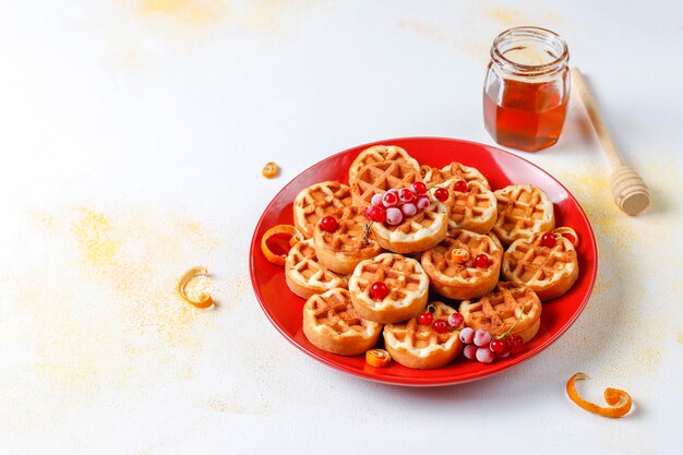 Waffles belgas tradicionales con miel y frutos rojos congelados.