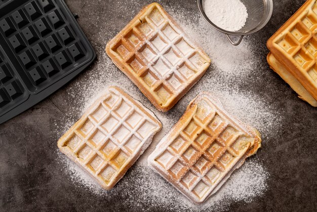 Waffles cubiertos de azúcar en polvo con waflera y tamiz