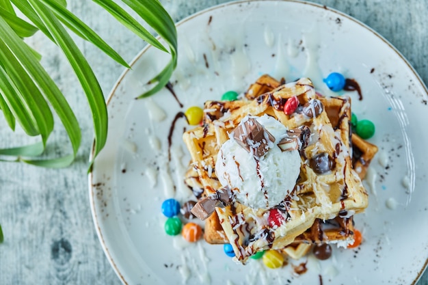 Waffles con helado, caramelo, chocolate en el plato blanco sobre la superficie de la hoja