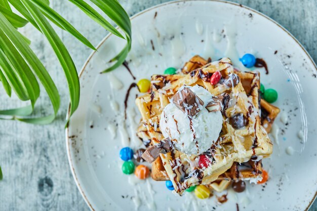 Waffles con helado, caramelo, chocolate en el plato blanco sobre la superficie de la hoja