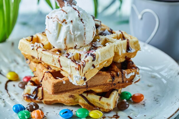 Waffles con helado, chocolate, bolas de chocolate en el plato blanco con té