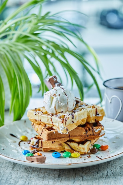 Waffles con helado, chocolate, bolas de chocolate en el plato blanco con té