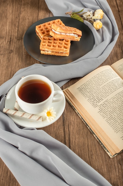 Waffles en un plato negro, una taza de té y un libro.