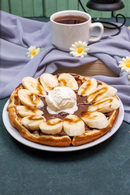 Waffles con rodajas de plátano, salsa de caramelo y crema batida con una taza de té