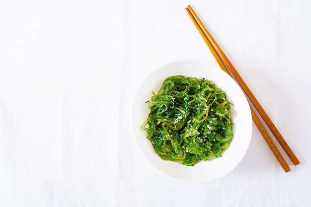 Wakame Chuka o ensalada de algas con semillas de sésamo en un recipiente en la mesa blanca. Comida tradicional japonesa Vista superior. Lay Flat