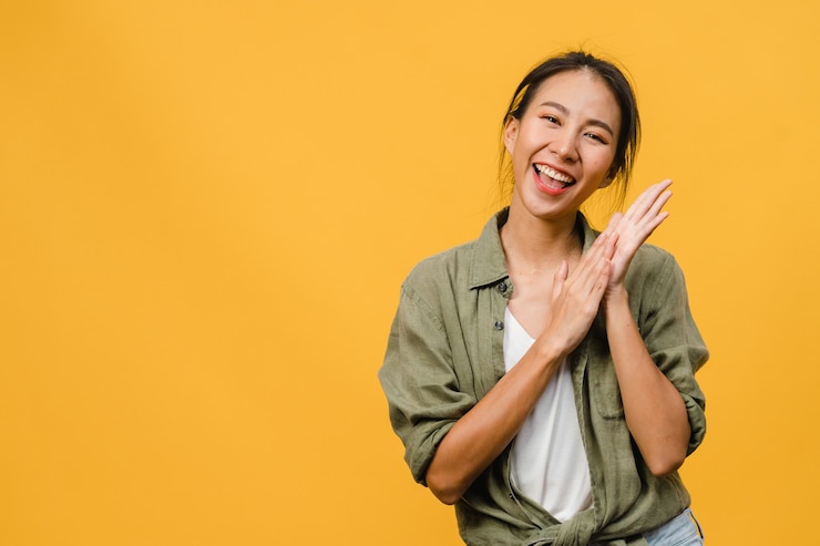 Photo Gratis wanita asia muda dengan ekspresi positif, tersenyum lebar, mengenakan pakaian kasual di depan dinding kuning. wanita bahagia dan menggemaskan bersukacita atas kesuksesan. konsep ekspresi wajah.