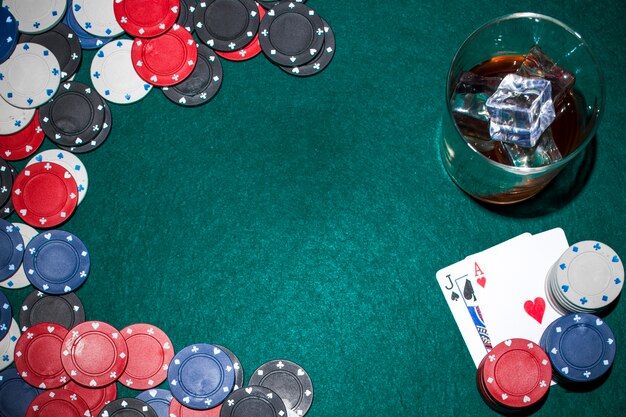 Whisky con cubitos de hielo y fichas de casino y naipes en la mesa de póquer verde