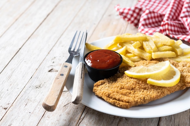 Wiener schnitzel con patatas fritas sobre mesa de madera