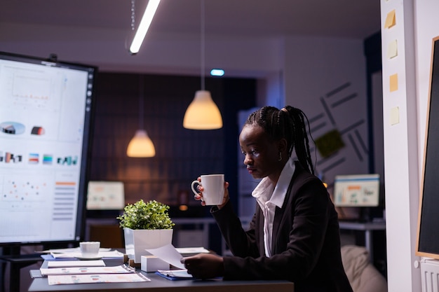 Workaholic empresaria afroamericana analizando estadísticas de marketing sobre trámites