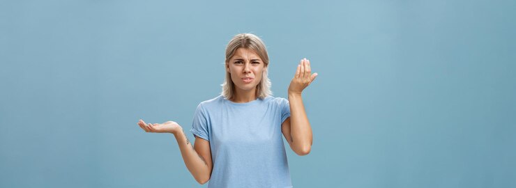 Foto gratuito wtf usted dice retrato de enojado y confundido novia elegante con cabello rubio levantando la palma alta y a un lado con expresión perpleja siendo cuestionado escuchando tonterías estúpidas sobre la pared azul