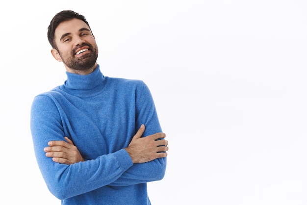 Éxito empresarial y concepto de finanzas Retrato de un apuesto hombre de negocios caucásico con cuello alto azul riéndose y cruzando las manos en los brazos se ve complacido y seguro de sí mismo de pie en el fondo blanco