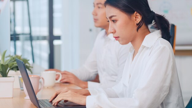 Éxito hermoso ejecutivo Asia joven empresaria elegante ropa casual viendo tutorial sobre ideas creativas en la computadora portátil durante el proceso de trabajo en el lugar de trabajo de la oficina moderna.