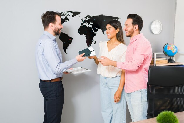 Ya está todo listo para sus vacaciones. Representante de ventas entregando pasaportes y boletos de avión a una mujer y un hombre jóvenes para su viaje de vacaciones en la agencia de viajes