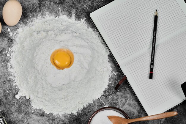 Yema de huevo en harina, cuaderno y lápiz sobre mesa de piedra.