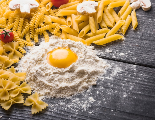 Yema de huevo en harina con diferentes tipos de pasta cruda en tablones de madera