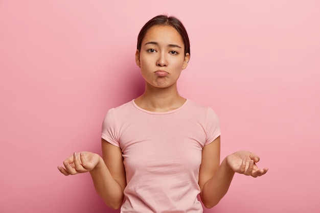 Yo no sé. Inconsciente, perpleja joven asiática extiende las palmas hacia los lados, no tiene idea de qué hacer, vestida con una camiseta informal, mira con tristeza, piensa cómo actuar en una situación problemática