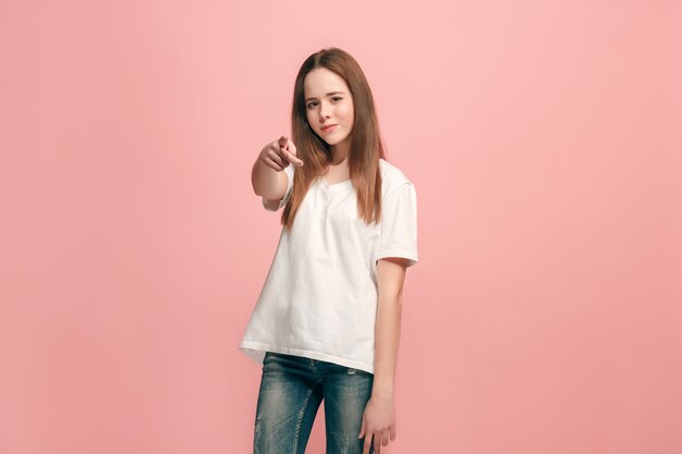 Yo te elijo y orden. La muchacha adolescente sonriente apuntando a la cámara, retrato de detalle de media longitud sobre fondo rosa de estudio. Las emociones humanas, el concepto de expresión facial. Vista frontal. Colores de moda